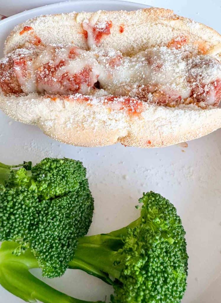 A meatball sub and broccoli on a blate.