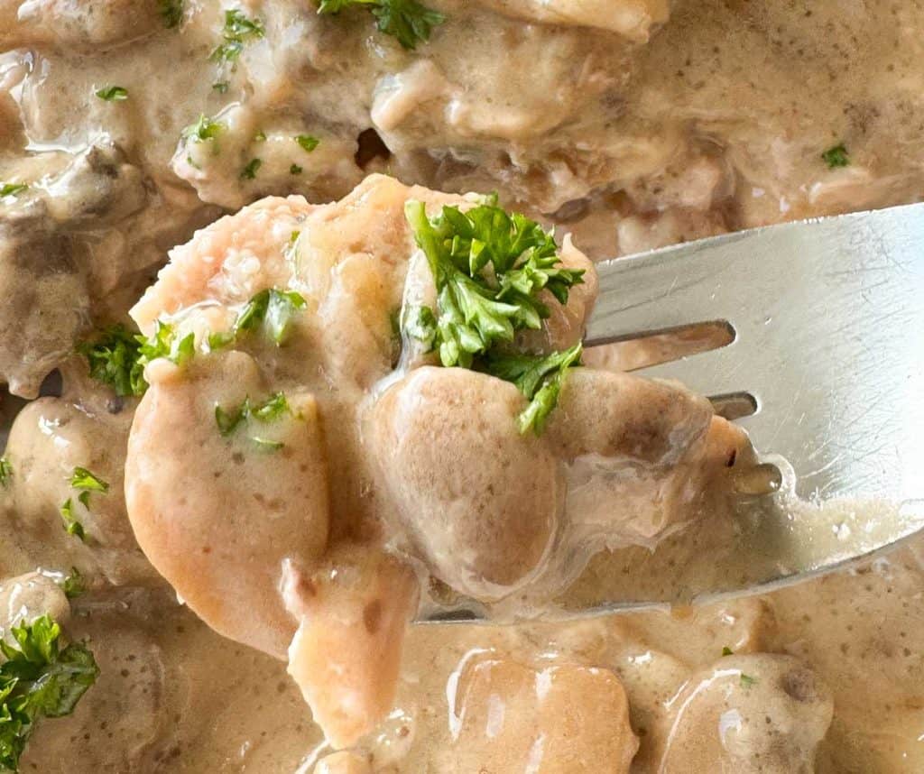 A bite of pork chops, mushrooms, and gravy on a fork.