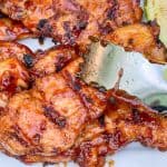 A pair of tongs picking up chicken.