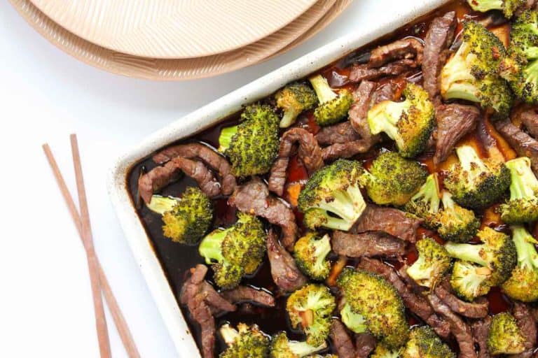 Beef and broccoli on a pan with plates and chopsticks.