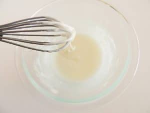 Whisk with icing dripping into a glass bowl of glaze.