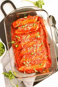 Baked 3 Cheese Manicotti in a dish with sauce, basil, and Parmesan.