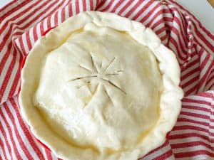 An unbaked apple pie with a puff pastry crust, brushed with an egg wash.