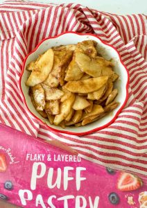 The prepared apple filling in the pie dish, with a package of puff pastry in the foreground.