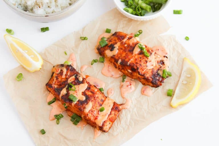 Plated Bang Bang Salmon topped with sauce, green onions, and served with rice.