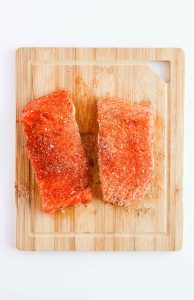 Two salmon fillets seasoned on a cutting board.