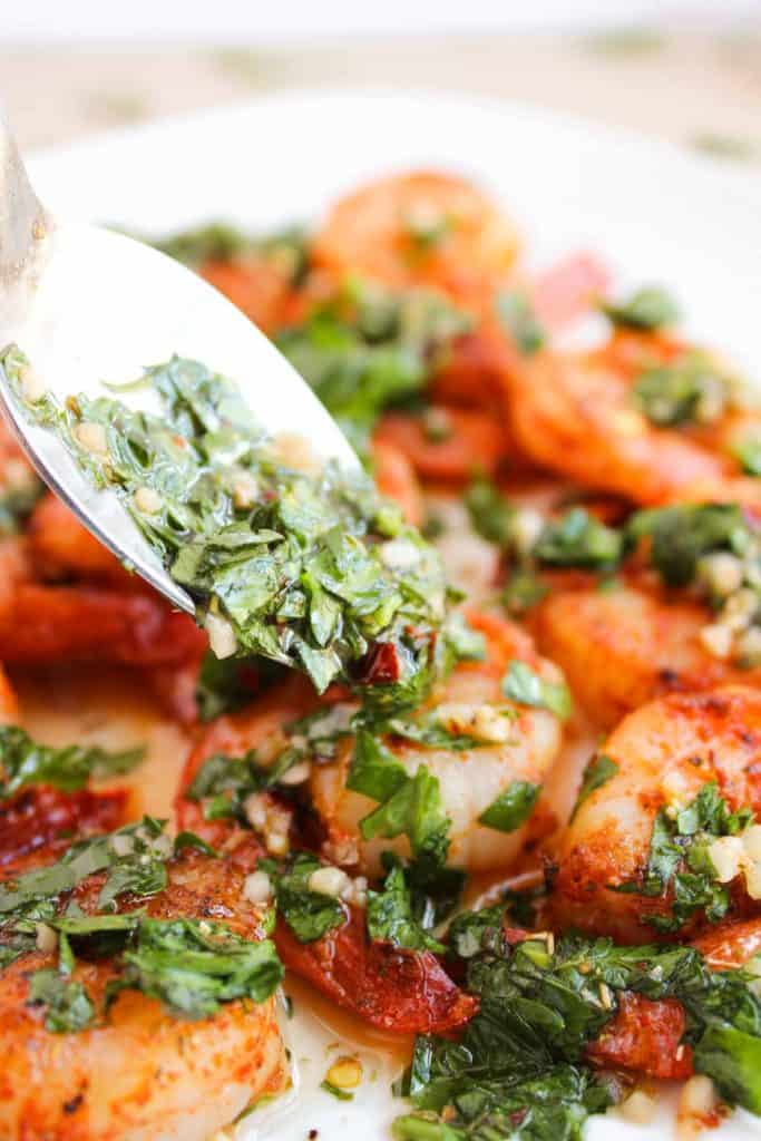 A spoon drizzling fresh chimichurri sauce over Chimichurri Shrimp on a plate.