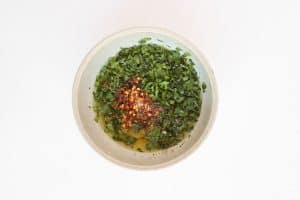 Chili flakes added to a bowl of Chimichurri Shrimp.
