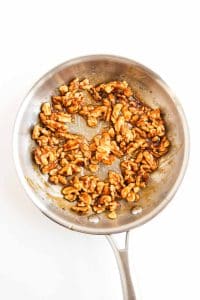 Candied walnuts coated in honey glaze in a pan.