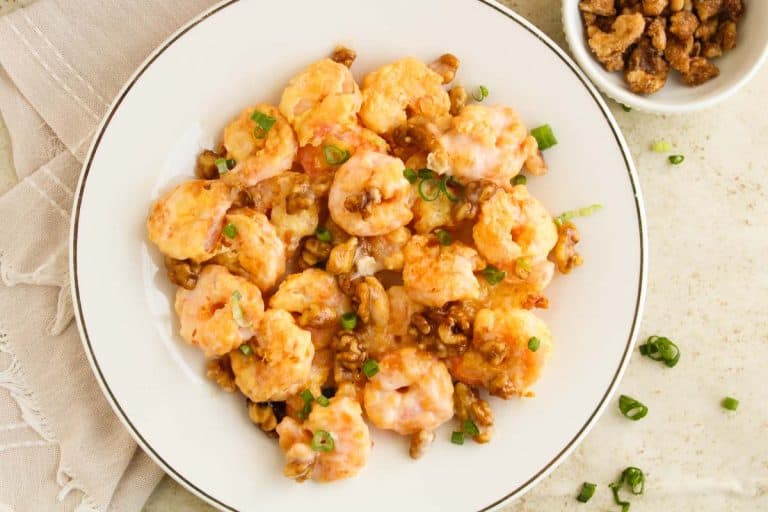 Close-up of plated honey walnut shrimp with a bowl of walnuts.