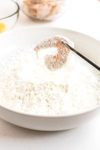 Shrimp coated in cornstarch held over a bowl.