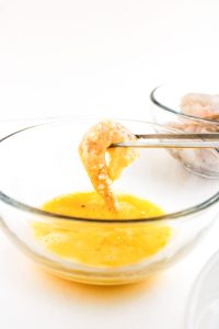 Shrimp dipped in beaten egg with tongs.