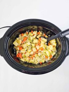 Vegetables for Corned Beeg Hash in the slow cooker stirred together with a black spoon.