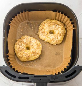 Uncooked sesame-topped bagels in the air fryer basket.