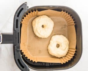 Two shaped bagels in an air fryer basket lined with parchment.