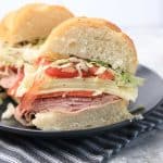 Halved Italian grinder sandwich showing layers of meat, cheese, tomato, and lettuce.
