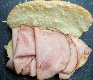 Open sandwich roll with several slices of deli ham layered on the bottom half.