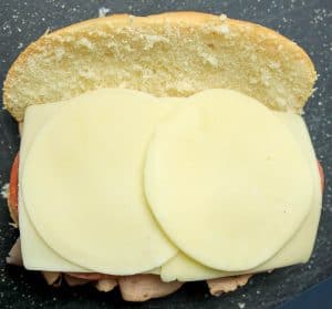 Slices of provolone cheese placed over the deli meats on the sandwich roll.