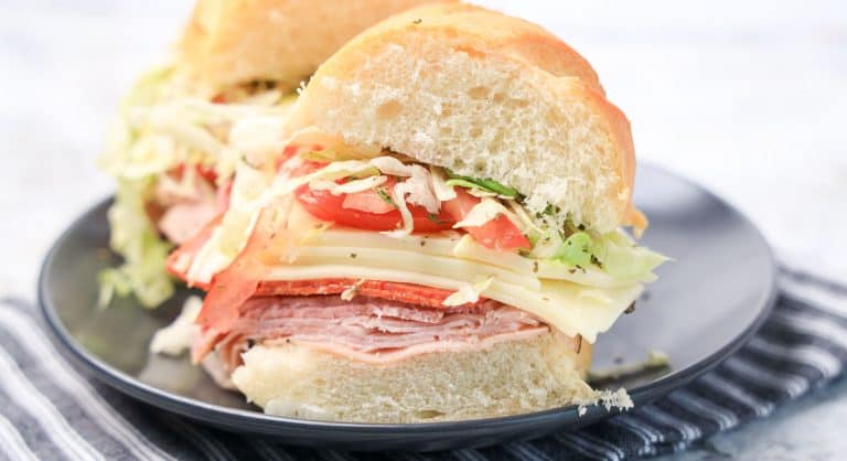 Halved Italian grinder sandwich showing layers of meat, cheese, tomato, and lettuce.