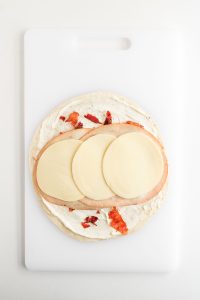 Provolone cheese and deli turkey are added over the tortilla with cream cheese mixture and crushed bacons.