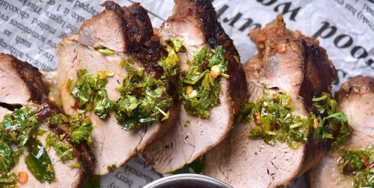 Close-up of grilled pork tenderloin slices with a thick coating of chimichurri sauce.