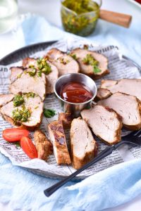 Pork tenderloin slices garnished with chimichurri, with a small dish of ketchup in the center.