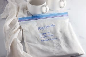 Bag of homemade white mug cake mix with instructions, next to two mugs.