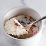 White mug cake with sprinkles on a spoon.