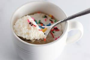 White mug cake with sprinkles on a spoon.