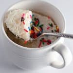 White mug cake with sprinkles on a spoon.
