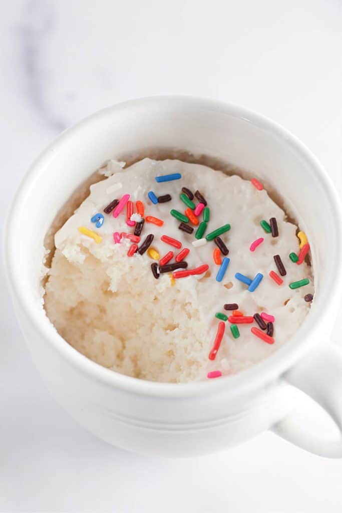 White mug cake topped with colorful sprinkles.
