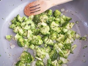 Chopped broccoli cooking with onions in a pan.