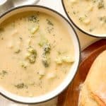 Overhead of two bowls of broccoli cheese soup with bread.