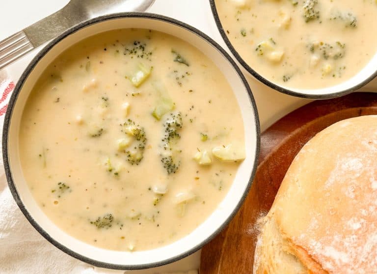 Overhead of two bowls of broccoli cheese soup with bread.
