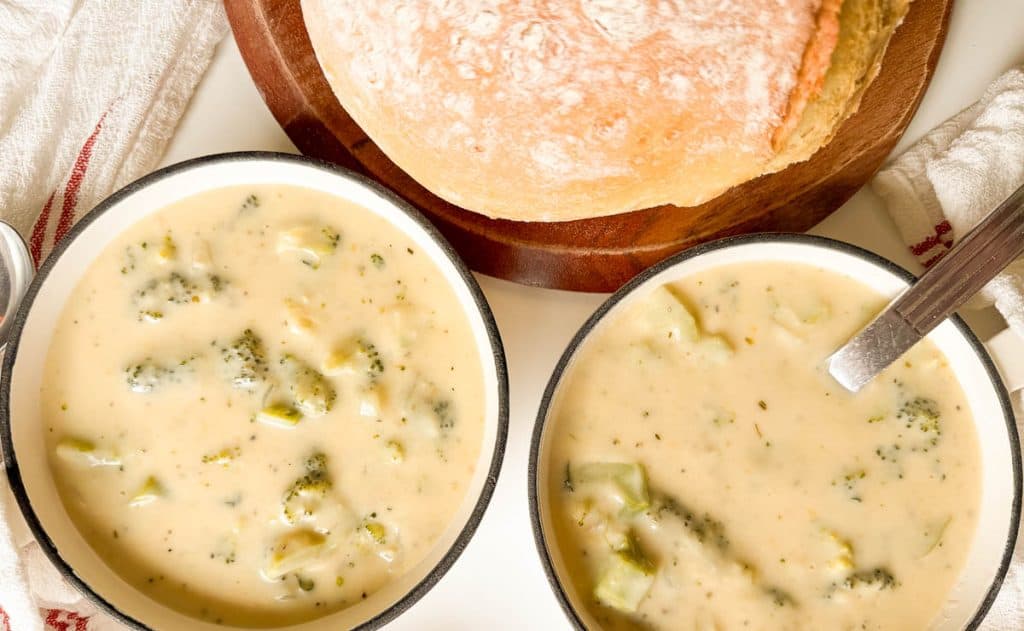 Overhead of two bowls of broccoli cheese soup with bread.