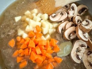 Diced potatoes, carrots, and sliced mushrooms added to the broth.