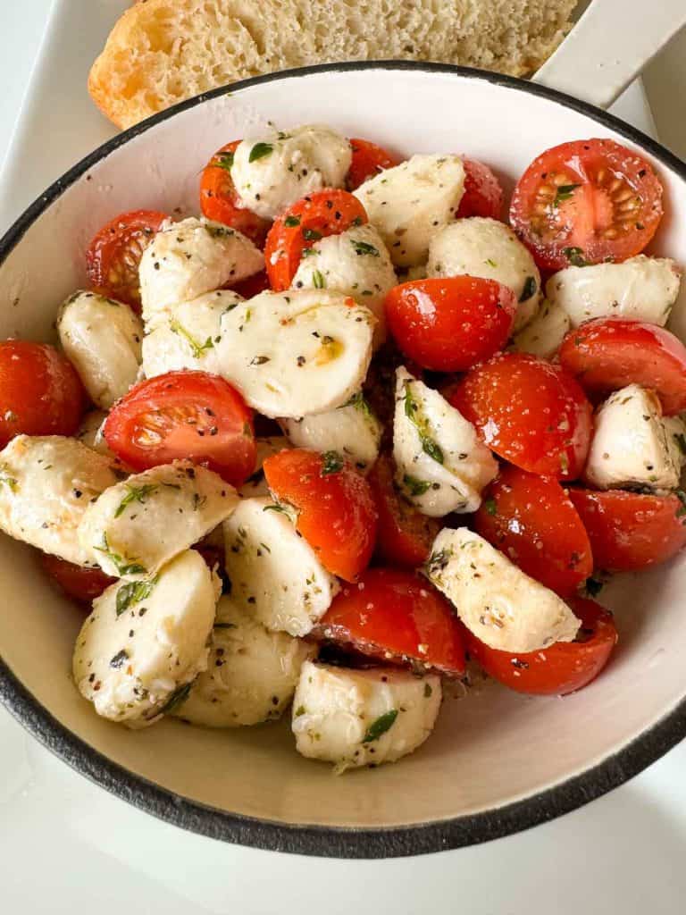 Bowl of mozzarella tomato salad with bread on the side.