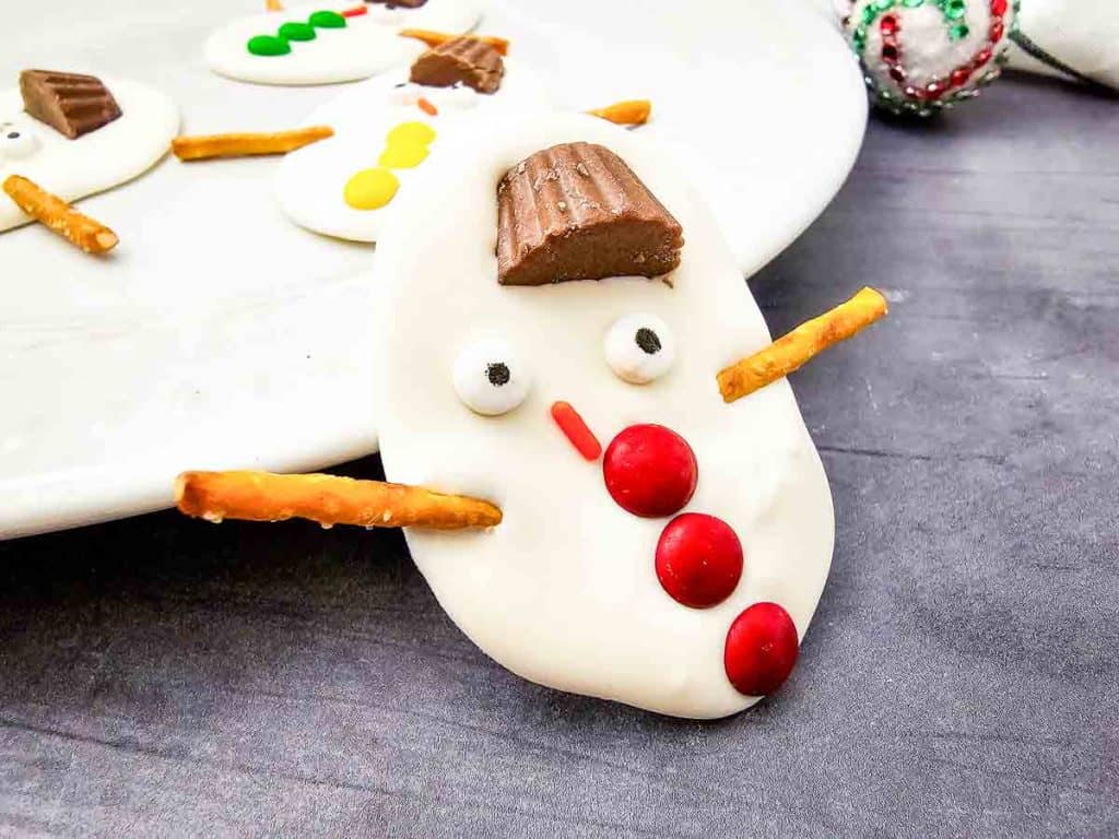 A melted snowman bark with red candy buttons leaning against a plate.