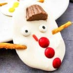 Close-up of a melted snowman bark with red buttons, candy eyes, and a peanut butter cup hat.