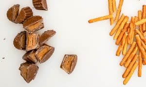Chopped peanut butter cups and pretzel sticks on a white surface.