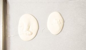 Two ovals of melted white chocolate on parchment paper.