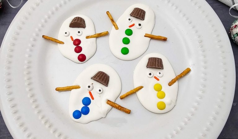 Four decorated melted snowman bark pieces on a white plate.