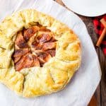 Baked apple galette with apple and cinnamon sticks beside it.