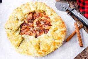 Overhead of galette with apple, cinnamon sticks, and pizza cutter.
