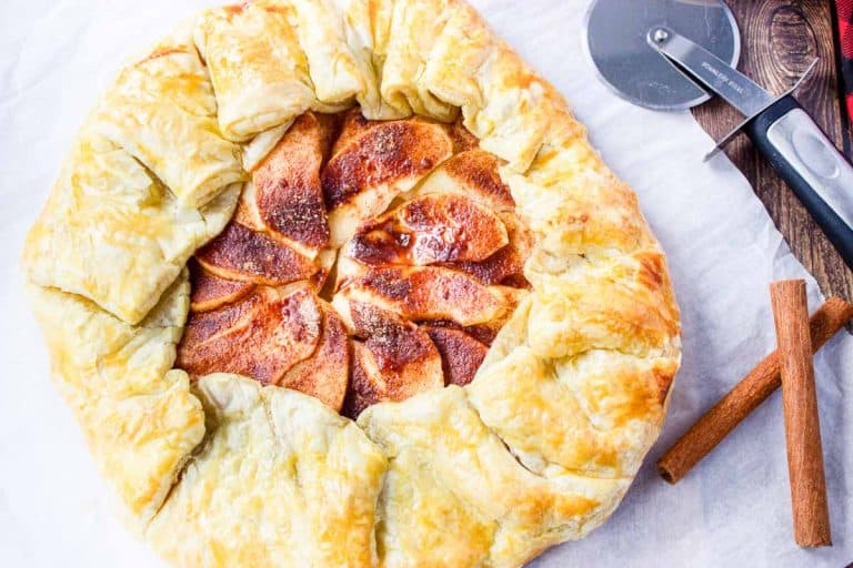 Overhead of galette with apple, cinnamon sticks, and pizza cutter.