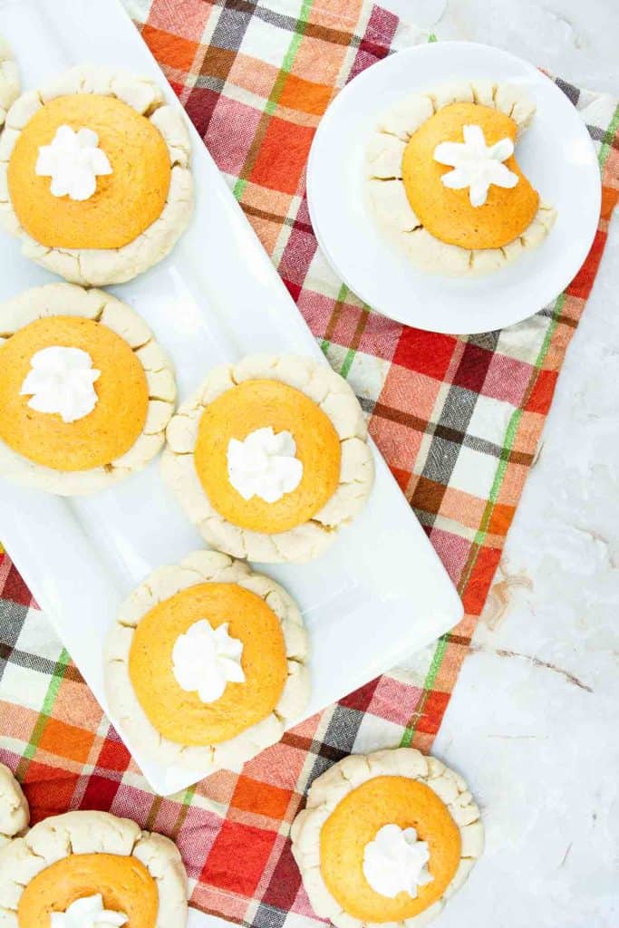 Pumpkin pie cookies with whipped cream on a plaid cloth.