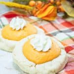 Two pumpkin pie cookies with whipped cream on a plaid cloth.