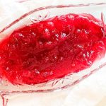 Overhead view of a glass serving dish filled with bright red cranberry sauce.