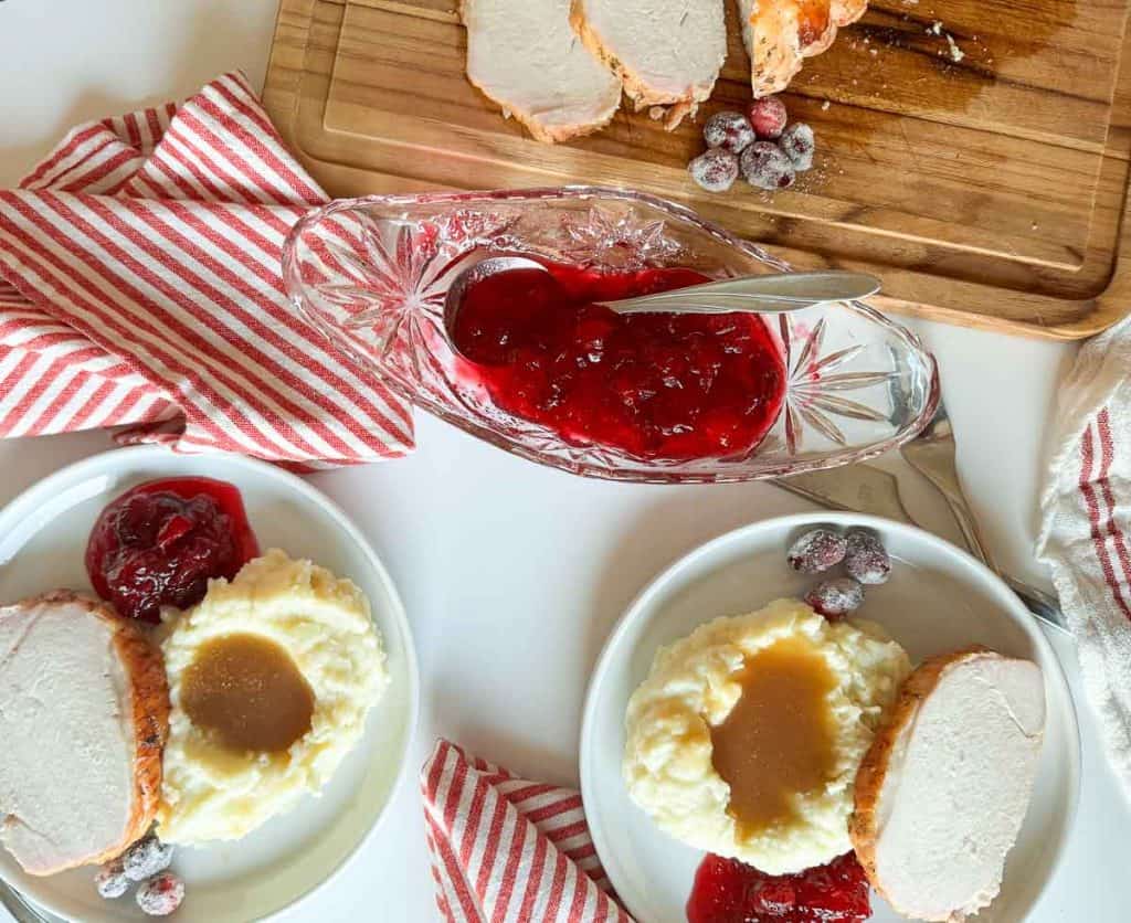 Overhead setup showing turkey plates, striped napkins, cranberry sauce, and sliced turkey on a board.
