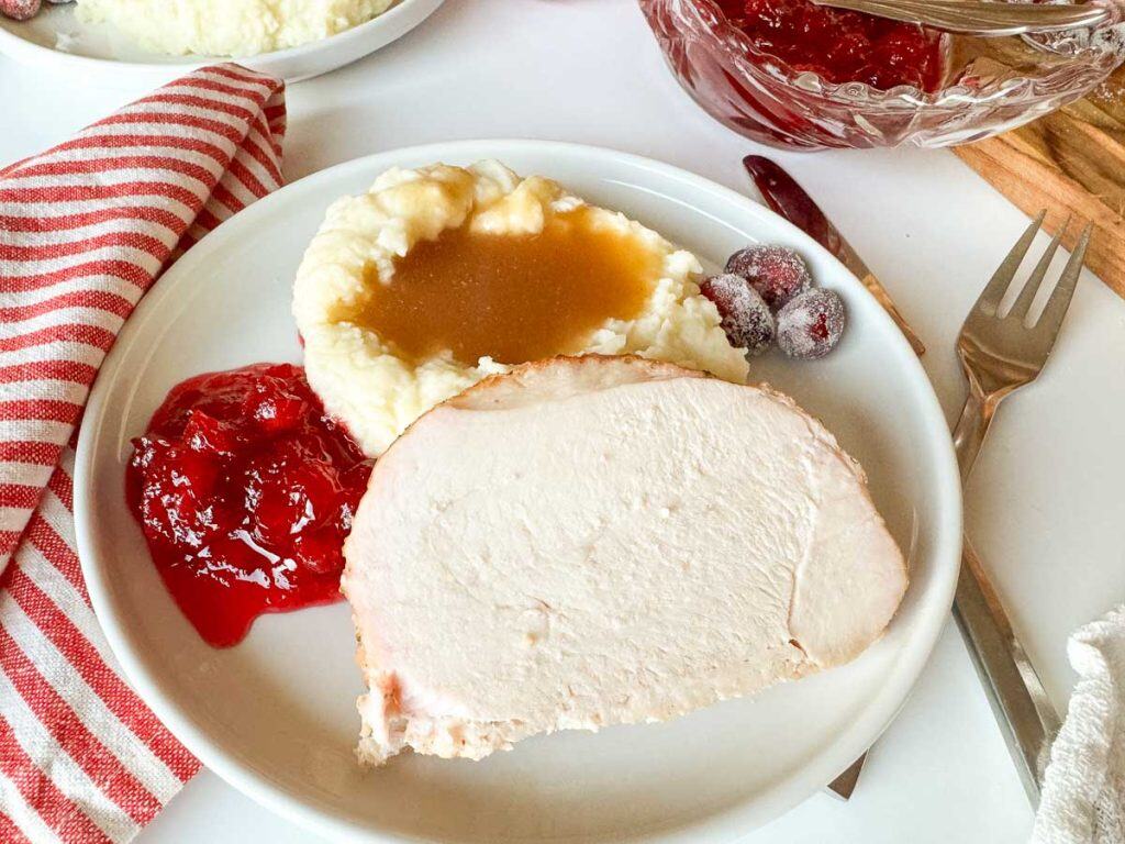 Turkey dinner plate with utensils and cranberry sauce in the background.
